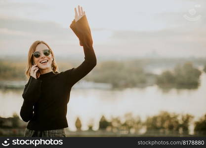 Portrait of young woman holding mobile phone while standing on walkway by the river