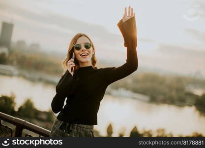 Portrait of young woman holding mobile phone while standing on walkway by the river