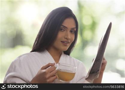 Portrait of young woman holding newspaper while drinking tea