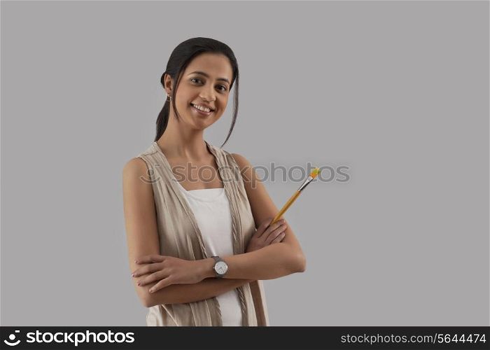 Portrait of young woman holding paintbrush isolated over gray background