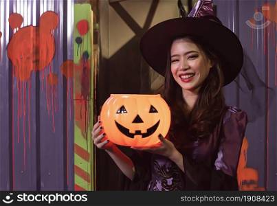 Portrait of young woman holding pumpkin and dressing halloween witch costume