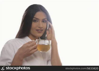 Portrait of young woman holding tea cup while using mobile phone