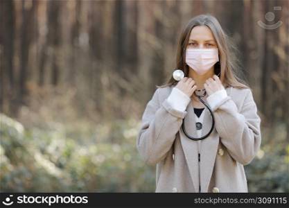 portrait of young woman in a face protective mask- girl with stethoscope around the neck-image of beautiful lady outdoors. copy space. portrait of young woman in a face protective mask- girl with stethoscope around the neck-image of beautiful lady outdoors. copy space.