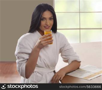 Portrait of young woman in bathrobe drinking orange juice at dining table