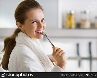 Portrait of young woman in bathrobe eating breakfast in morning