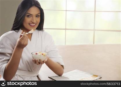 Portrait of young woman in bathrobe having breakfast at dining table