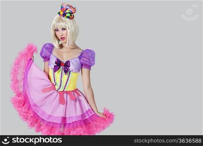 Portrait of young woman in doll&acute;s costume posing against gray background