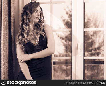 Portrait of young woman in lingerie.. Portrait of woman looking through french door window at home. Attractive young girl with long hair in lingerie. Female fashion.