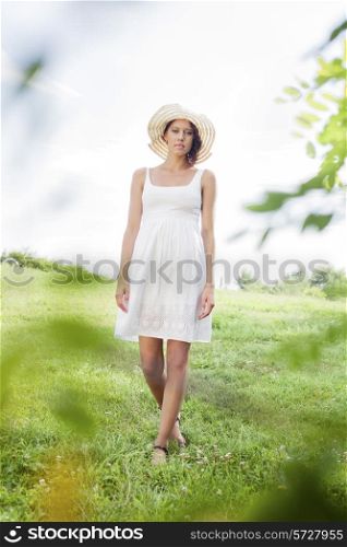 Portrait of young woman in sundress and hat walking in park