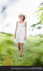 Portrait of young woman in sundress and hat walking in park