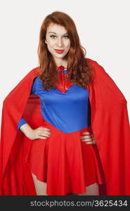 Portrait of young woman in superhero costume with hands on hips against gray background