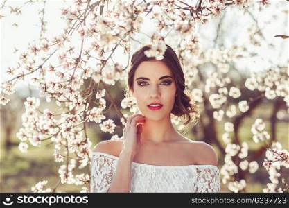 Portrait of young woman in the flowered garden in the spring time. Almond flowers blossoms