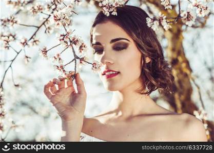 Portrait of young woman in the flowered garden in the spring time. Almond flowers blossoms. Girl dressed in white like a bride.