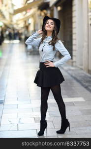 Portrait of young woman in urban background wearing casual clothes and hat carrying a bag