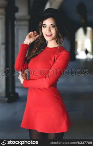 Portrait of young woman in urban background wearing red dress and hat