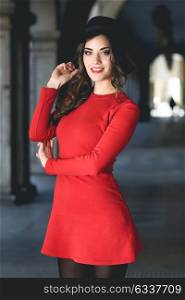 Portrait of young woman in urban background wearing red dress and hat