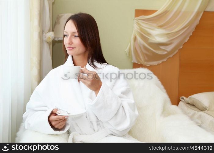 portrait of young woman in white bath robe holding a cup of tea