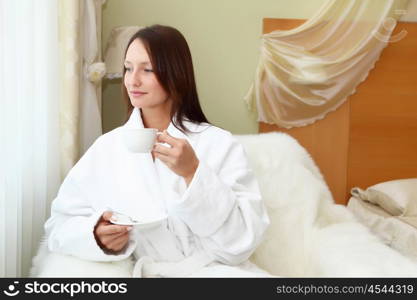 portrait of young woman in white bath robe holding a cup of tea