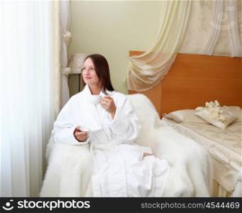 portrait of young woman in white bath robe holding a cup of tea