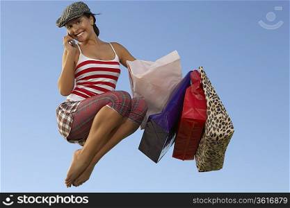 Portrait of young woman jumping with shopping bags, using mobile