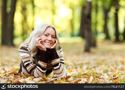 Portrait of young woman laying on ground with autumn leaves in park. Woman in autumn park