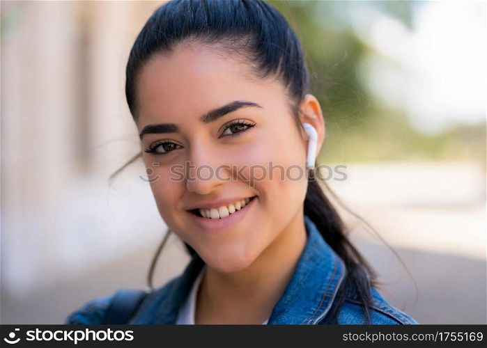 Portrait of young woman listening to music with earpods while standing outdoors on the street. Urban concept.