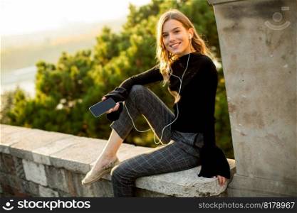 Portrait of young woman listens to music from a mobile phone outside