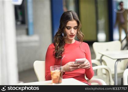 Portrait of young woman looking at her smart phone sitting in a cafe bar having a drink