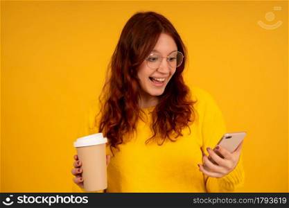 Portrait of young woman looking at the mobile phone with shocked expression while standing against isolated background.