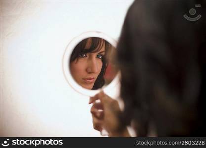 Portrait of young woman looking in handheld mirror