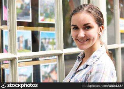 Portrait Of Young Woman Looking In Window Of Estate Agent