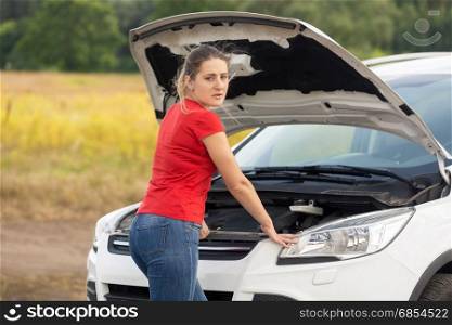 Portrait of young woman looking under the hood of broken car