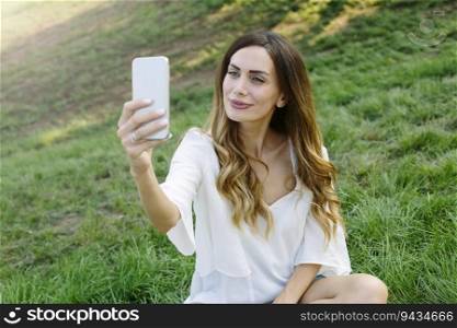 Portrait of young woman making selfie photo in park on summer day