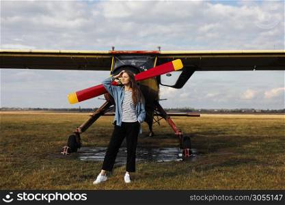 portrait of young woman near the retro plane. field with plane flying over it. portrait of young woman near the retro plane. field with plane flying over it.
