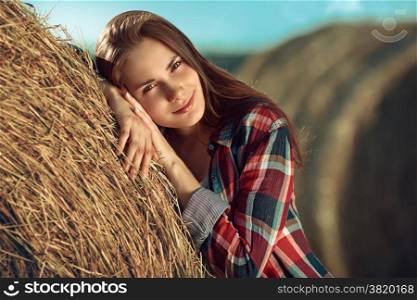 Portrait of young woman next to a stack of hay in sunlight