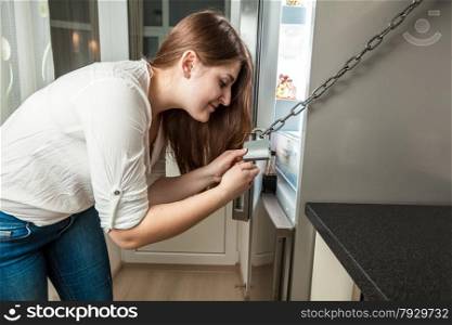 Portrait of young woman opening fridge locked by chain