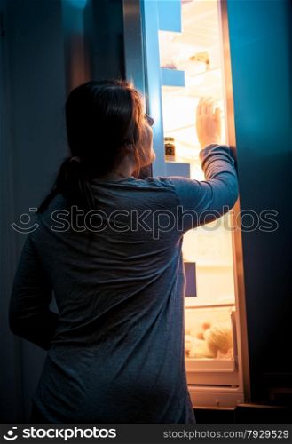 Portrait of young woman opening refrigerator at night