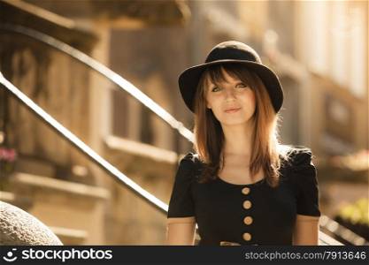 Portrait of young woman outdoors. Retro style fashion girl in black hat and dress on street of the old town european city Gdansk Danzig Poland