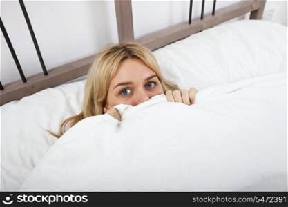 Portrait of young woman peeking over quilt