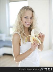 Portrait of young woman peeling banana in house