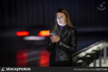 Portrait of young woman posing at road at night with mobile phone