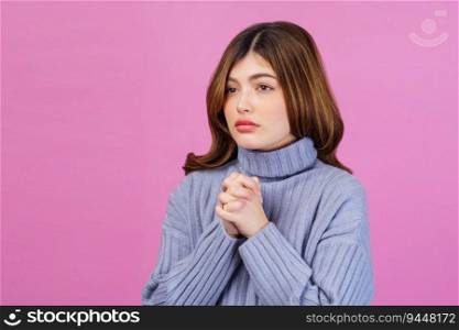 Portrait of young woman praying with folded hand or making a wish isolated over pink background. People lifestyle concept.