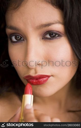 Portrait of young woman putting on red lipstick