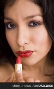 Portrait of young woman putting on red lipstick