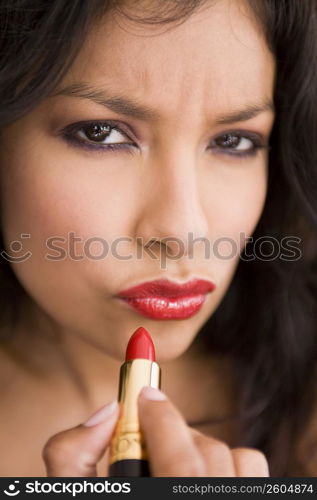 Portrait of young woman putting on red lipstick