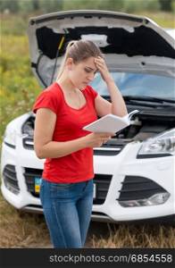 Portrait of young woman reading owner manual at broken car