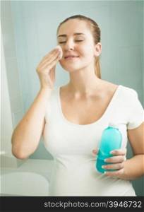 Portrait of young woman removing makeup with lotion and cotton pad