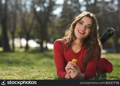 Portrait of young woman rest in the park smiling with a dandelion in her hair, lying on the grass