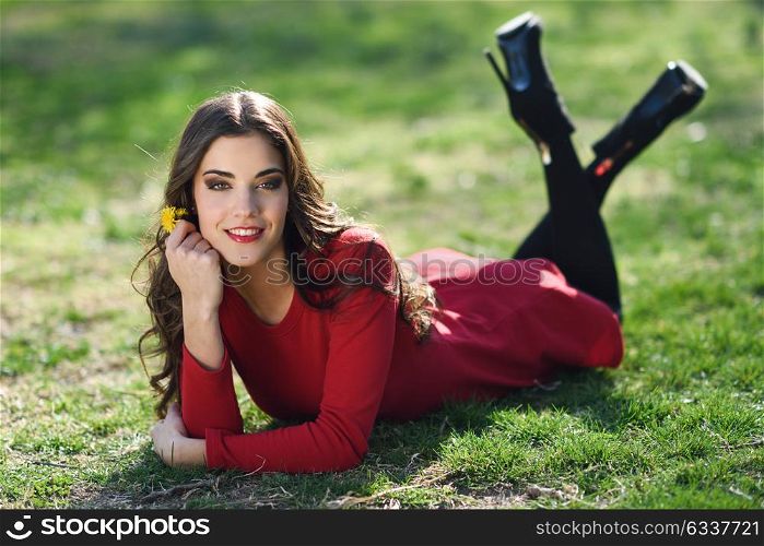 Portrait of young woman rest in the park smiling with a dandelion in her hair, lying on the grass