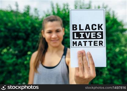 Portrait of young woman showing card against racism. Selective focus on card in foreground. Woman showing symbol of feminism